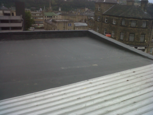 Flat commercial roof with a seamless black membrane, overlooking Pittsburgh's urban landscape, showcasing potential for durability and energy efficiency in roofing solutions.