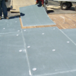 Workers installing roofing materials on a flat roof, demonstrating the repair process for tree damage with a focus on safety and structural integrity.