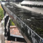 Gutter overflowing with water during rainfall, illustrating the importance of proper drainage in roofing and exterior maintenance.