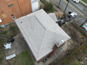 Aerial view of a residential roof with new shingles and surrounding landscape, illustrating components of a complete roof replacement as discussed in roofing installation guide.