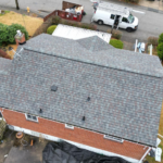Aerial view of a residential roof featuring Pinnacle® Sun Shingles, showcasing the shingles' design and color, with nearby landscaping and a service van visible.