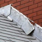 Roof flashing detail on a sloped roof, showing shingles and brick wall, relevant to gutter installation and maintenance.