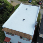 Flat white roof with two ventilation pipes, surrounded by greenery and residential buildings, illustrating modern roofing solutions in Pittsburgh.