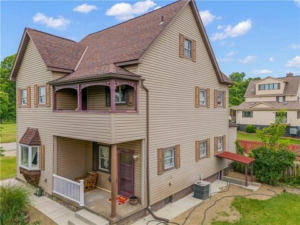 Two-story home with neutral siding, contrasting trim, and a welcoming porch, surrounded by green landscaping, illustrating ideal exterior color choices for enhancing curb appeal.