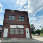 Brick building in Sheraden, Pittsburgh, with two doors and large windows, surrounded by a clear blue sky, relevant to winter roofing and home protection discussions.