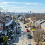 Historic homes lining a street in Shadyside, Pittsburgh, showcasing traditional architecture and modern vehicles, with a view of the city skyline in the background.