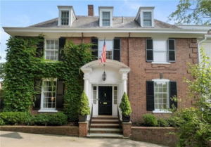 Elegant brick residential home with ivy-covered facade, featuring a central entrance, American flag, and manicured landscaping, emphasizing quality exterior solutions by Malick Brothers Exteriors.