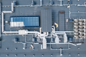 Aerial view of a commercial flat roof featuring HVAC units, ductwork, and a glass enclosure, illustrating components relevant to commercial roofing systems and maintenance considerations.