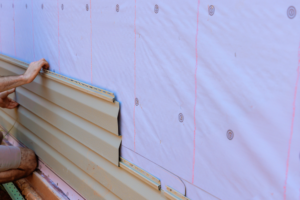 Person installing insulated siding onto exterior wall with foam backing, highlighting energy-efficient construction for homes in Pittsburgh's climate.