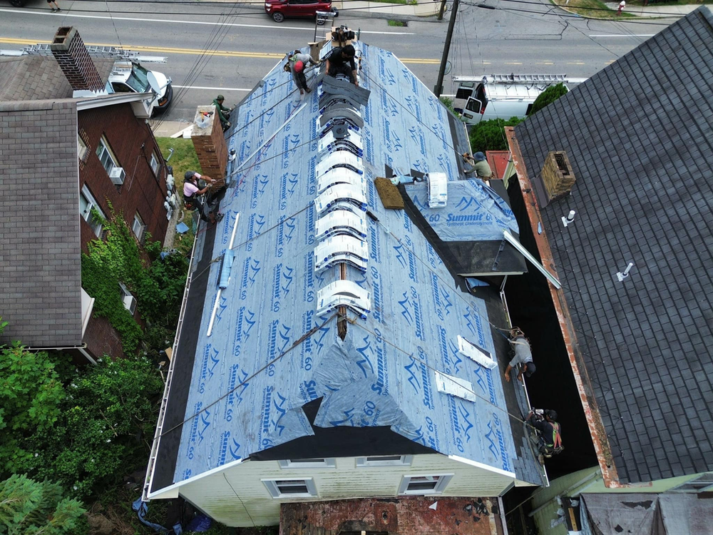 Roofers installing new shingles on a historic Pittsburgh home, showcasing roofing materials and techniques essential for maintaining architectural integrity.
