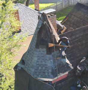 Roof installation with contractor working on complex turret design, showcasing premium shingles and ventilation considerations.