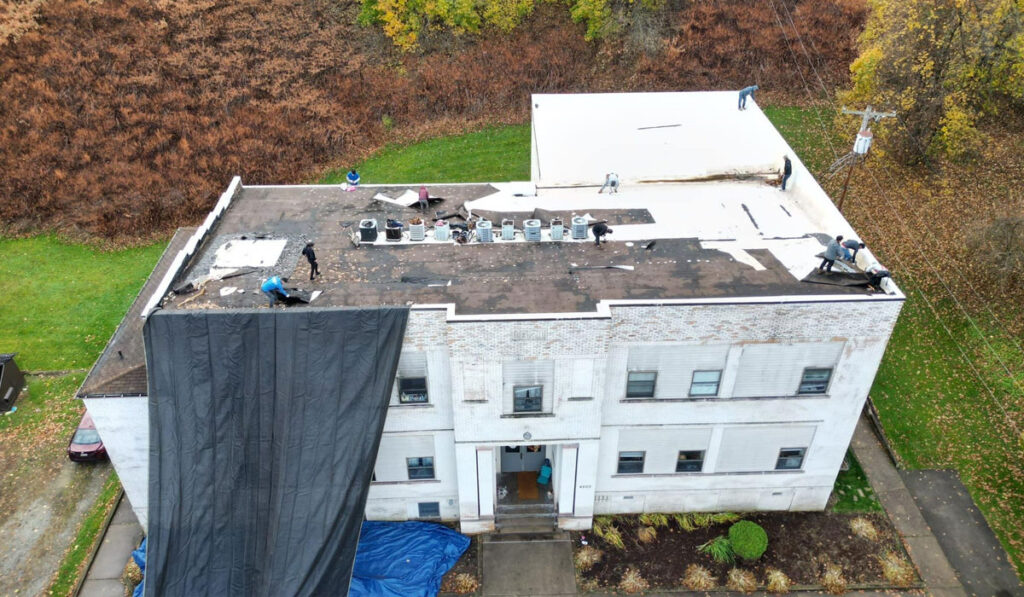 Commercial roof replacement in progress, workers removing old roofing material and applying a new membrane, showcasing proactive maintenance essential for longevity in Pittsburgh's climate.