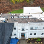 Commercial roof replacement in progress, workers on flat roof, visible roofing materials and tarps, Pittsburgh area building.