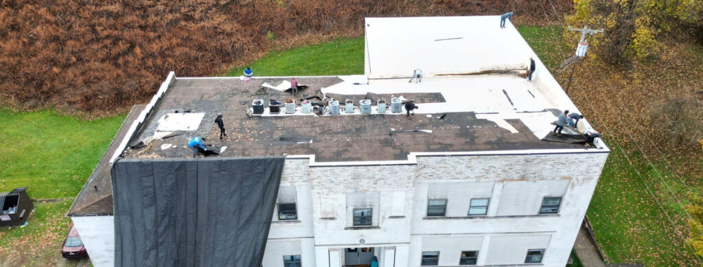Roofing crew performing commercial roof replacement on a building, with tarps and equipment visible, emphasizing proactive maintenance for fall weather preparedness in Pittsburgh.