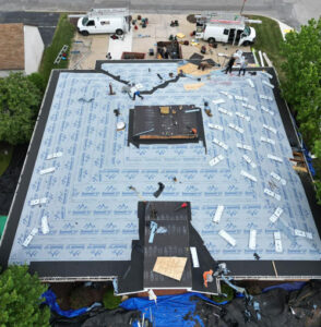 Commercial roofing installation in progress, featuring workers applying materials on a flat roof with insulation and protective layers, surrounded by equipment and vehicles.
