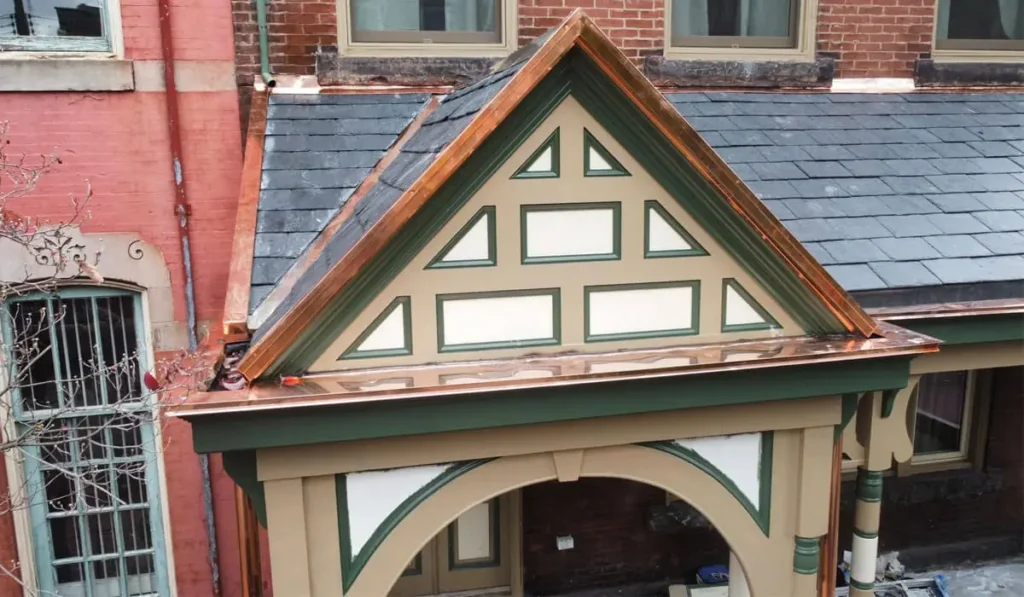 Slate roofing installation with decorative trim and copper flashing on a historic building, showcasing longevity and maintenance aspects of roofing materials.