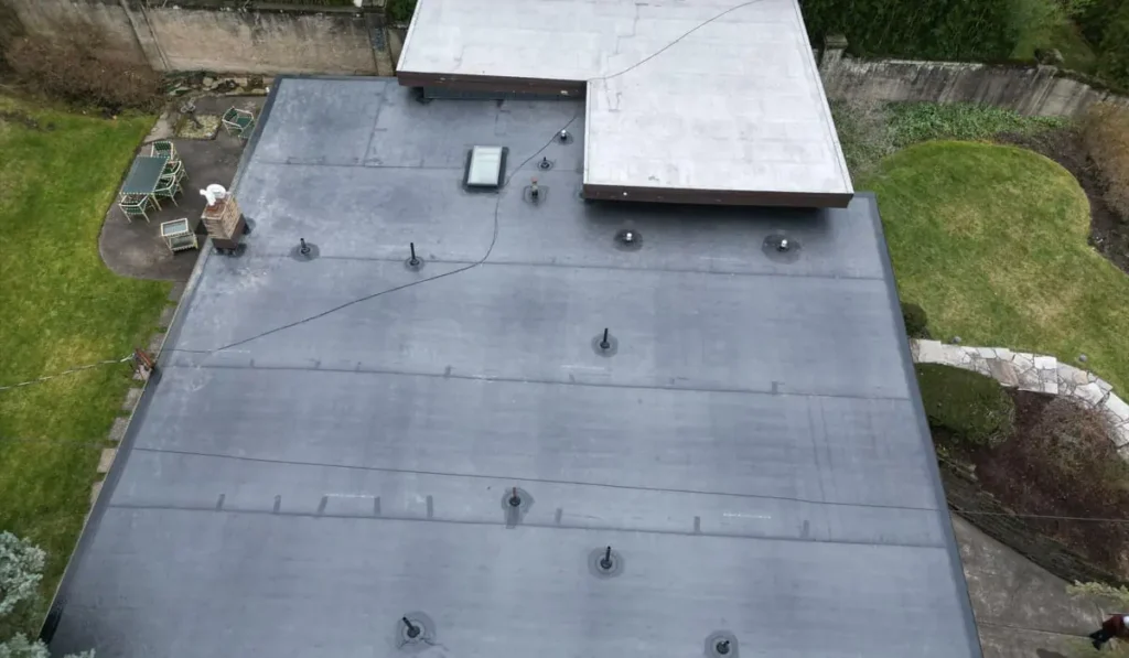 Flat commercial roof covered with EPDM membrane, showcasing black rubber surface, drainage features, and skylight, surrounded by green lawn and patio furniture.