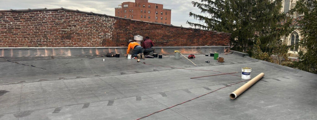 Workers applying EPDM roofing on a commercial building, showcasing insulation layers and tools for installation, with a brick wall backdrop.