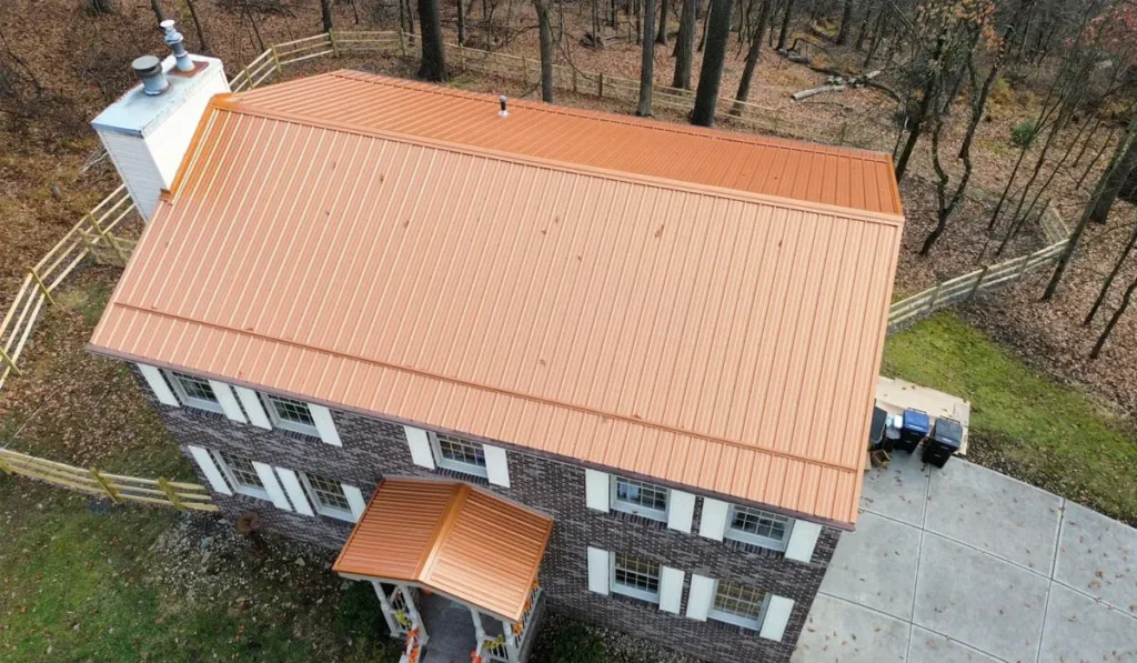 Aerial view of a residential building featuring a newly installed orange metal roof, surrounded by trees and a fenced yard, highlighting Malick Brothers Exteriors' metal roofing services in Pittsburgh.