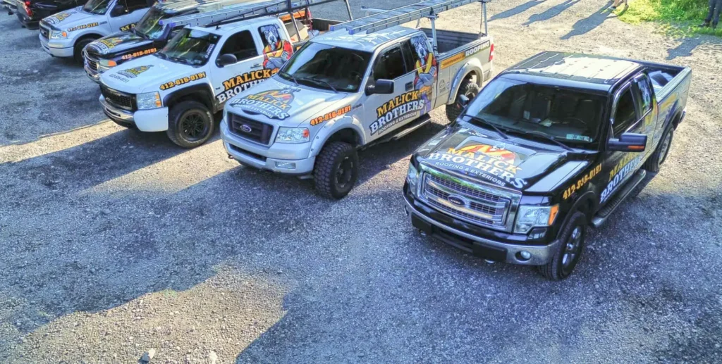 Malick Brothers Exteriors branded trucks parked in a gravel lot, showcasing their roofing services in Pittsburgh.