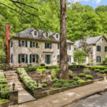 Elegant residential home with green shutters, surrounded by lush landscaping and trees, showcasing potential roofing needs for Pittsburgh homeowners.