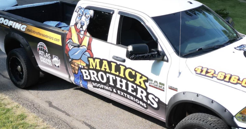 Malick Brothers Exteriors branded truck featuring a cartoon dog mascot, promoting roofing services, parked on a residential street.