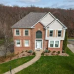Two-story brick house with a well-maintained lawn, surrounded by trees, illustrating residential roofing in Pittsburgh's climate.