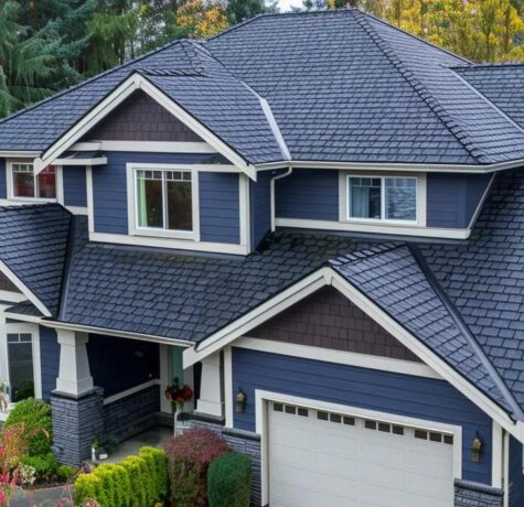 Aerial view of a modern home featuring a dark shingle roof, blue siding, and well-maintained landscaping, relevant to roofing solutions for homeowners in Pittsburgh.