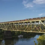 Soaring high above Harmar Township, PA, the southbound Bessemer and Lake Erie ore train from Conneaut crosses the massive bridge over the Allegheny River as it nears North Bessemer. The crew will leave their106 loads at the yard for the Union Railroad and return north with more empty hoppers for the ore dock on Lake Erie. Power for today's train is IC SD70's 1018 and 1034 along with CN SD60 5422.