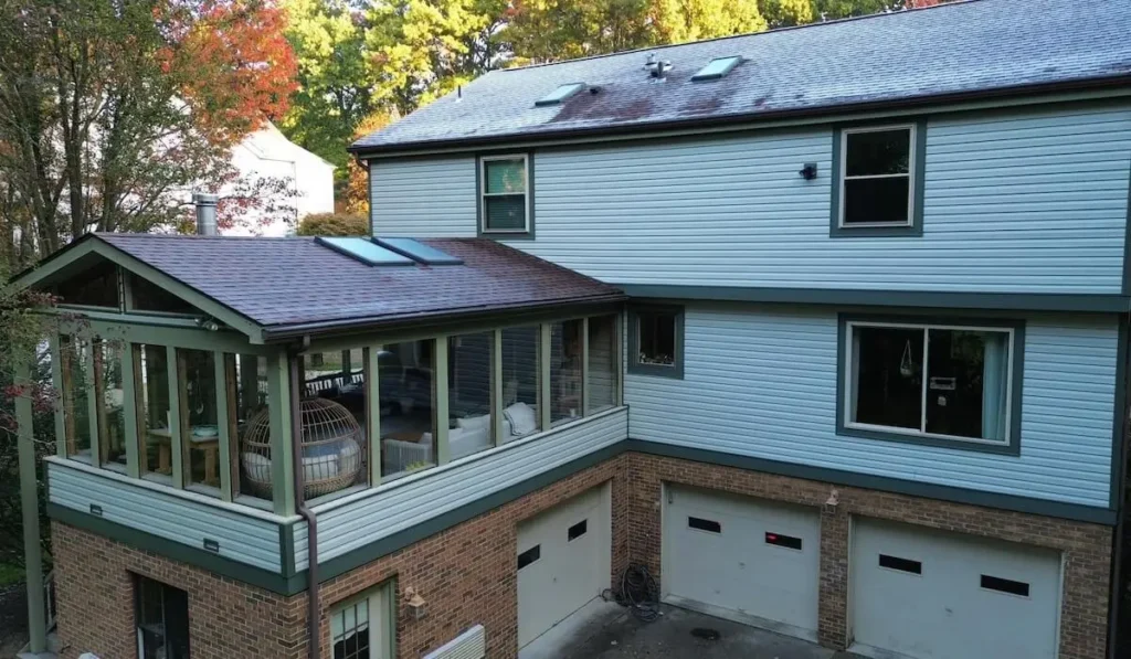 House exterior featuring a modern addition with a glass-enclosed porch, new roofing, and siding, highlighting quality craftsmanship by Malick Brothers Exteriors.