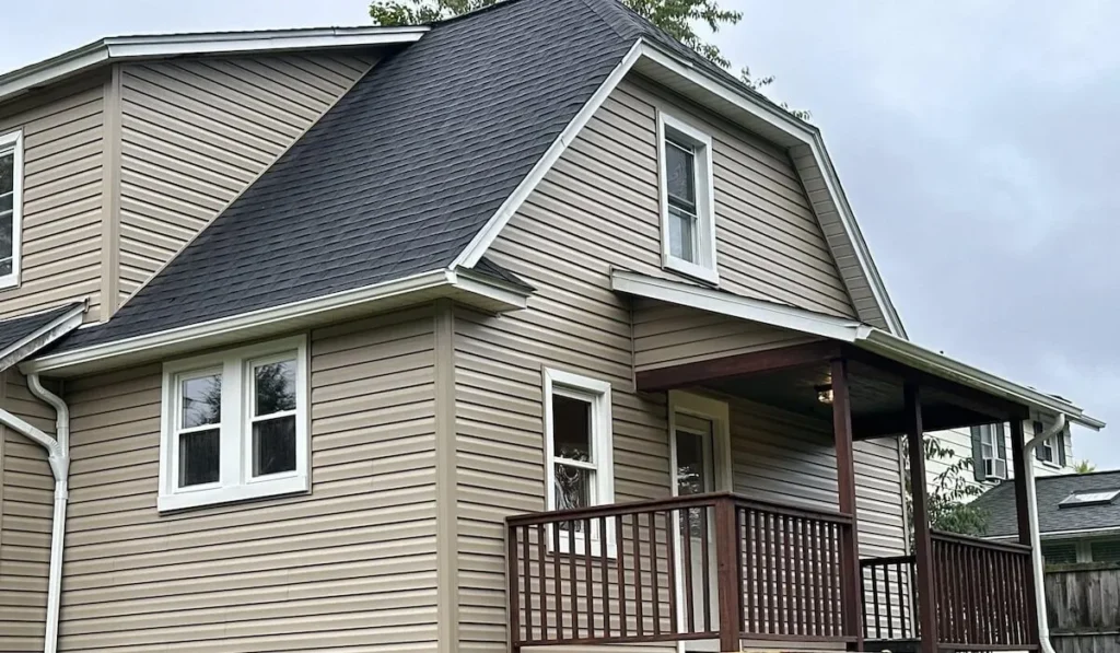 House exterior featuring a newly installed gray shingle roof, light brown siding, and a front porch, relevant to roofing and exterior solutions.