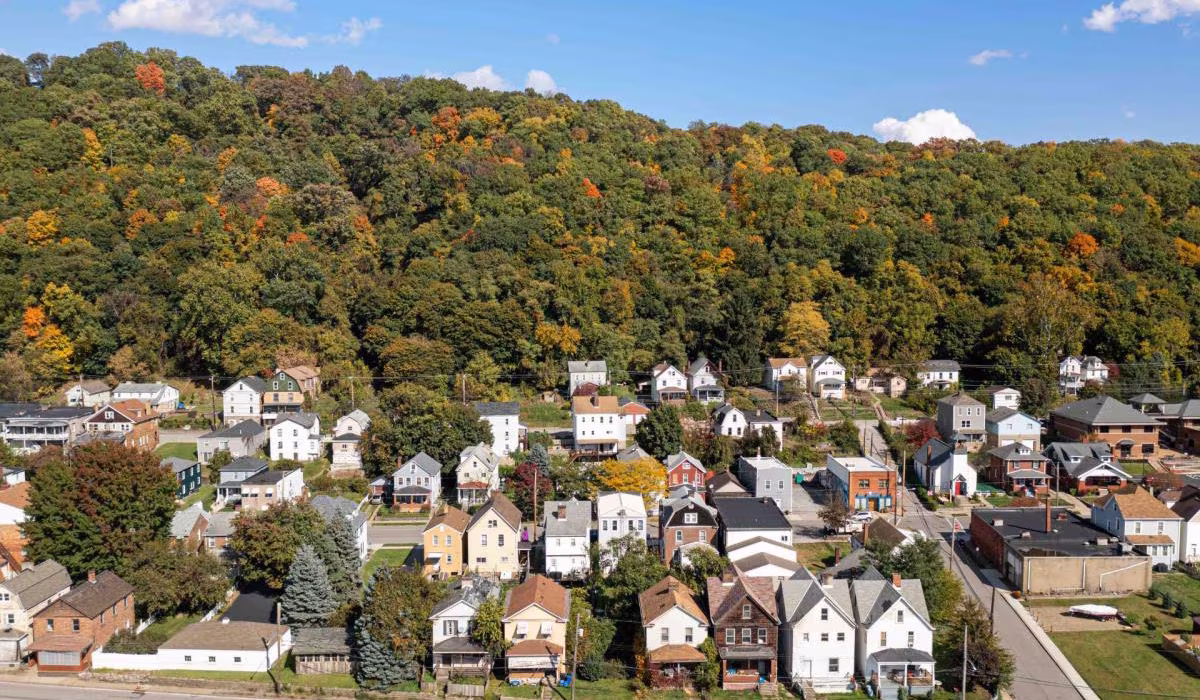 Aerial view of residential neighborhood in Pittsburgh, showcasing houses surrounded by autumn foliage and hills, relevant to roofing permits and inspections.