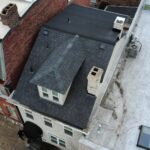 Aerial view of a residential roof in Pittsburgh featuring dark shingles, chimneys, and adjacent buildings, illustrating the importance of roof inspections and maintenance by Malick Brothers Exteriors.