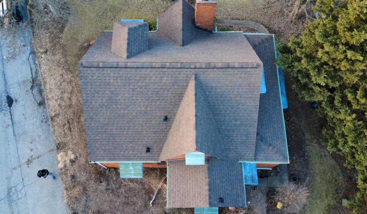 Aerial view of a residential home featuring a newly installed asphalt shingle roof, showcasing multiple gables and vents, surrounded by trees and a paved driveway, relevant to roofing material options for Pittsburgh's weather.