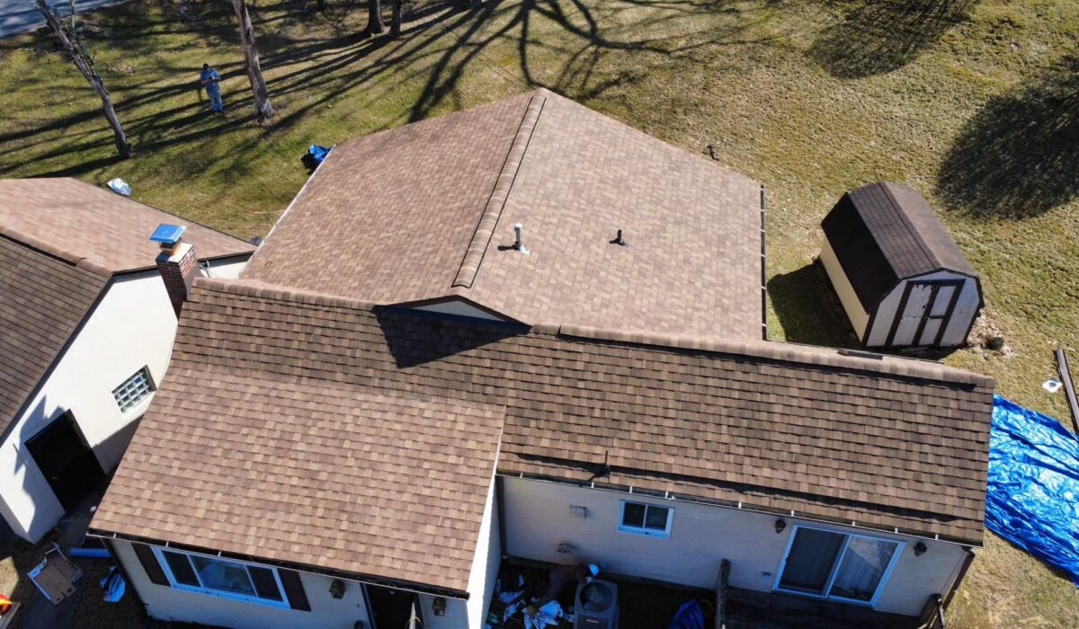 Aerial view of a newly installed roof with brown shingles on a residential home, showcasing the roofing project by Malick Brothers Exteriors, with a backyard and shed in the background.