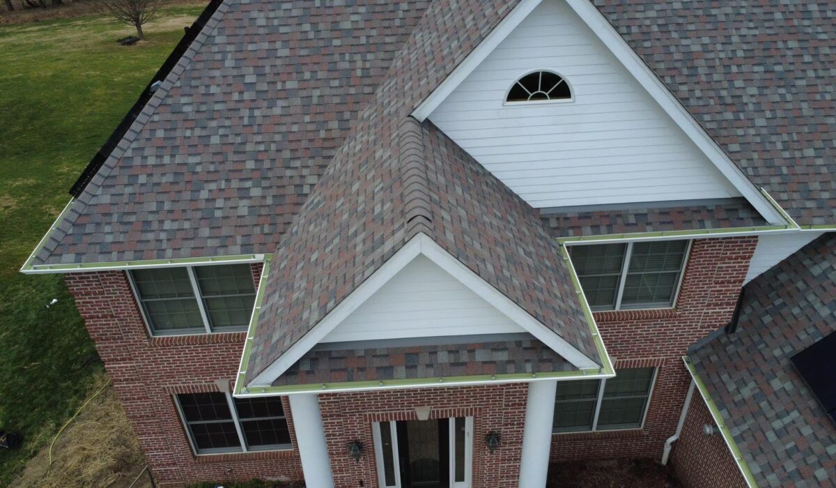 Newly installed asphalt shingle roof on a residential home in Pittsburgh, showcasing a combination of brown and gray shingles, with a gable design and brick exterior.