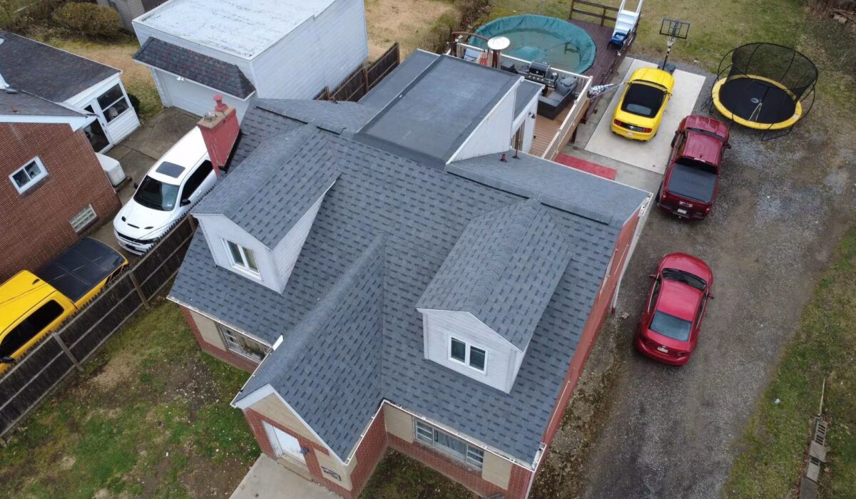 Aerial view of a residential home in Western Pennsylvania with a newly installed asphalt shingle roof, surrounded by parked vehicles and a trampoline, illustrating the importance of timely roof repairs.