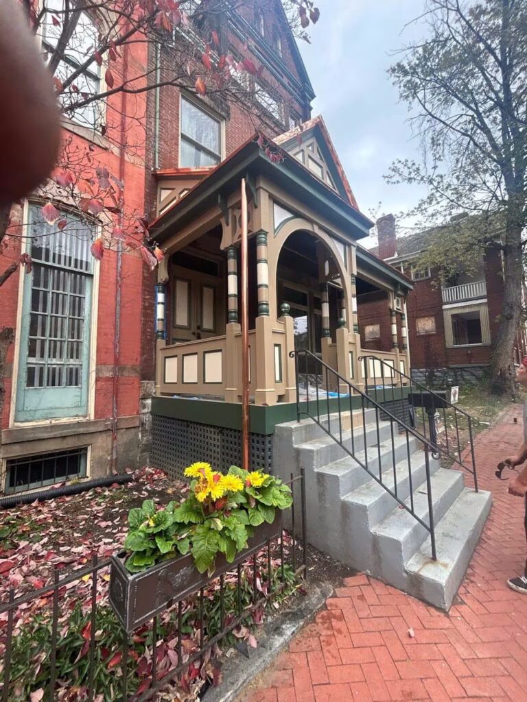 Victorian-style home exterior with muted color palette, featuring a decorative porch, landscaped flower bed, and brick pathway, illustrating luxury home aesthetics.