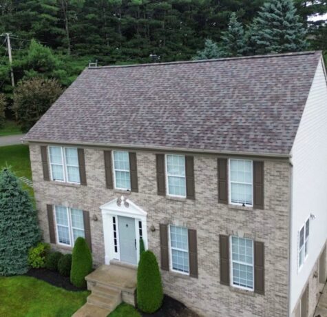 Residential home with new roofing and brick exterior, showcasing quality craftsmanship by Malick Brothers Exteriors, surrounded by green landscaping in Pittsburgh.
