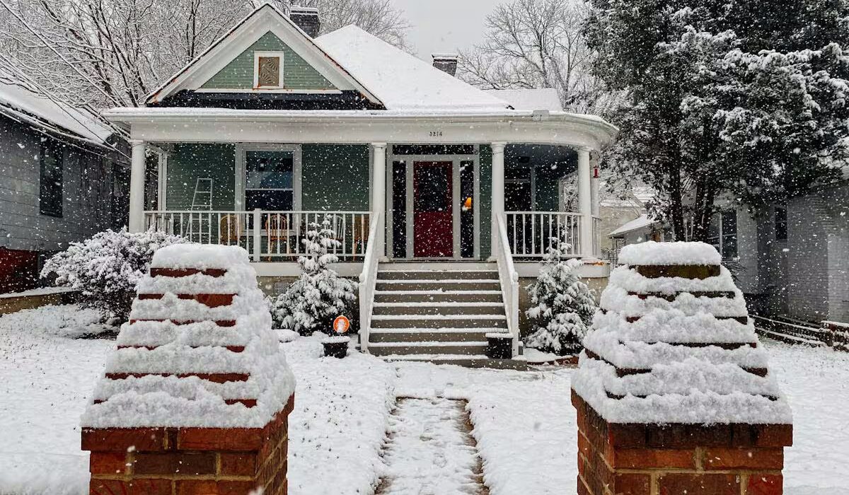 Snow-covered house in Pittsburgh with ice guard roofing, surrounded by winter scenery and decorative brick pillars.