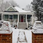 Snow-covered house with a flat roof in Pittsburgh, showcasing rubber roofing benefits in winter conditions, surrounded by a snowy pathway and brick pillars.