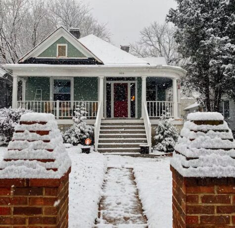 Snow-covered residential home with a welcoming porch, surrounded by winter scenery, highlighting exterior features relevant for roofing and maintenance discussions in Pittsburgh.