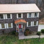 Two-story residential home with a copper roof and stone exterior, surrounded by greenery, illustrating effective roofing solutions for Pittsburgh homeowners.