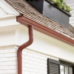 Roof edge with red gutter and downspout, showcasing proper drainage for effective roof ventilation in residential architecture.