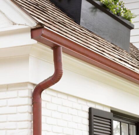 Roofing detail with red downspout and wooden shingles, highlighting gutter system important for Pittsburgh homeowners' storm preparation and maintenance.