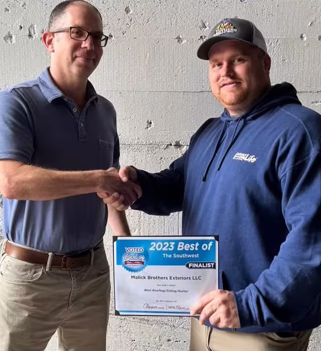 Men shaking hands in front of a concrete wall, holding a certificate for Malick Brothers Exteriors as a finalist for "2023 Best of the Southwest" in roofing and siding.