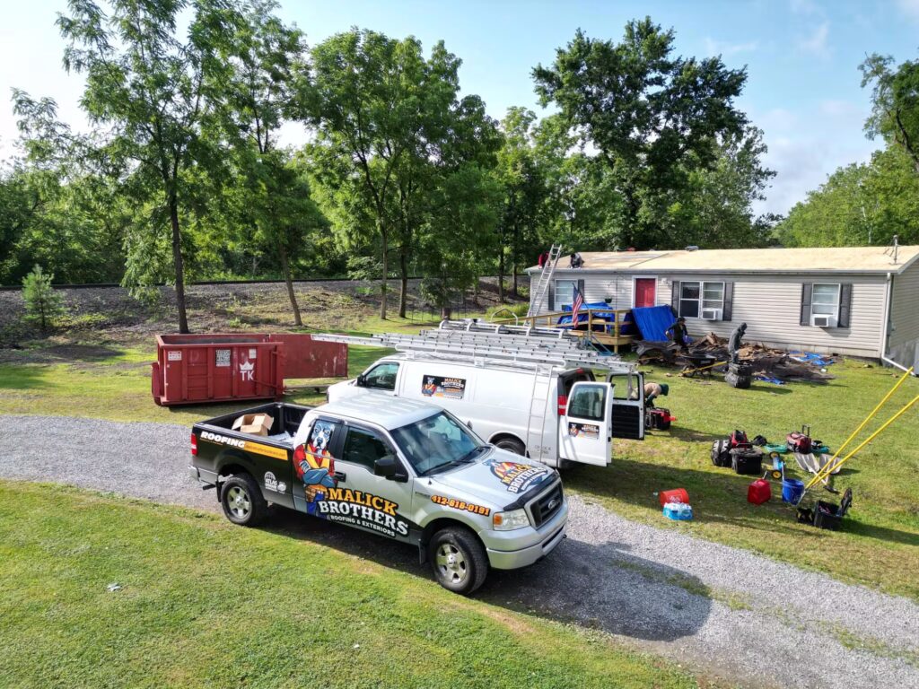 Malick Brothers Exteriors truck and van at a roofing job site in Pittsburgh, showcasing rubber roofing installation with tools and materials, surrounded by trees and a residential home.