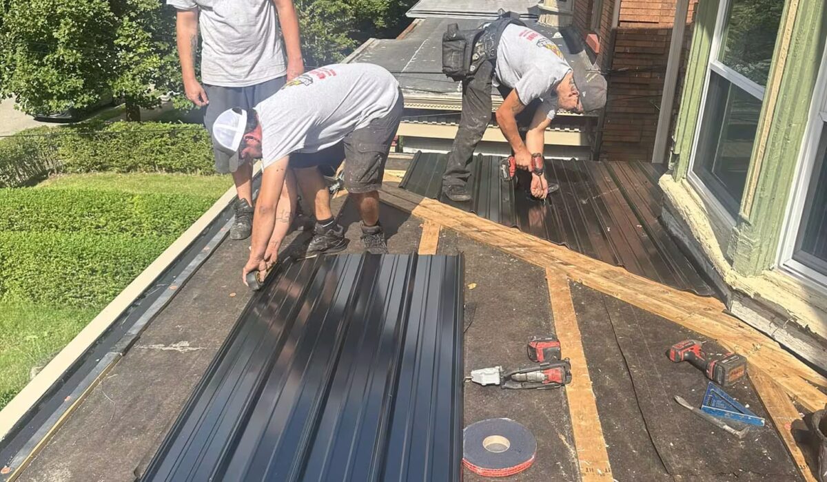 Three roofing contractors installing metal roofing panels on a residential roof, showcasing tools and materials used in roofing services.