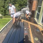 Three roofing professionals installing metal roofing panels on a residential roof in Pittsburgh, demonstrating skilled labor and precision in roofing services.