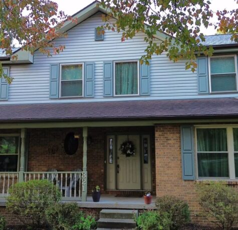 Two-story residential home with blue siding, green shutters, and a welcoming front porch, showcasing quality exterior craftsmanship relevant to Malick Brothers Exteriors' roofing and home improvement services.